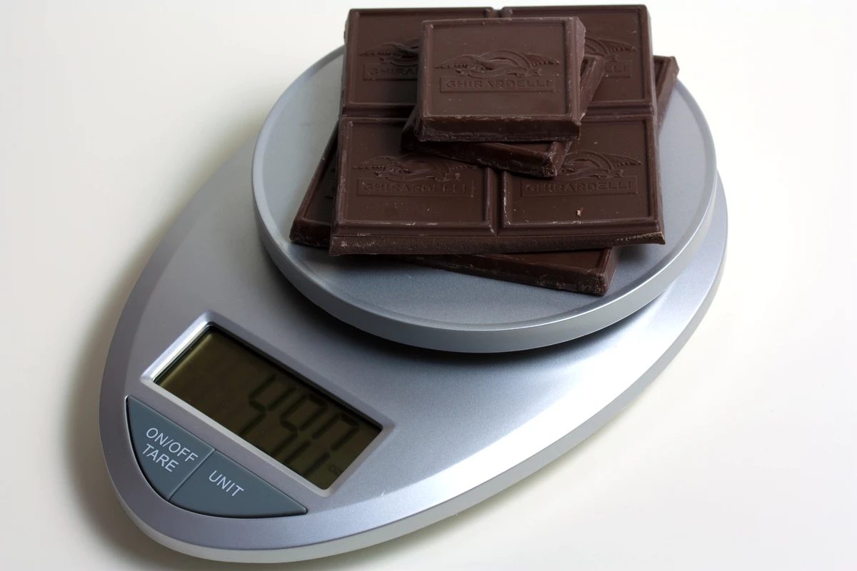 A digital kitchen scale weighing chocolate, with an on/off tare button beside the display